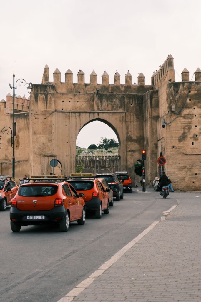 Historic city gate in Fes, Morocco, with red petit taxis and traffic passing through