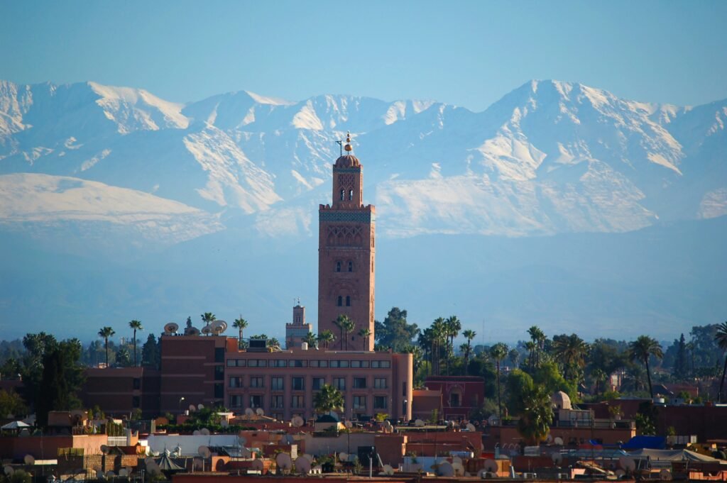 Koutoubia Mosque minaret in Marrakech with snow-capped Atlas Mountains — the best time to visit Morocco often means warm city days and cold peaks at once